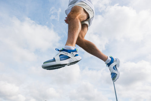 Athlete jumping in CUVS Whiteout track spike covers over blue sprint spikes outdoors.