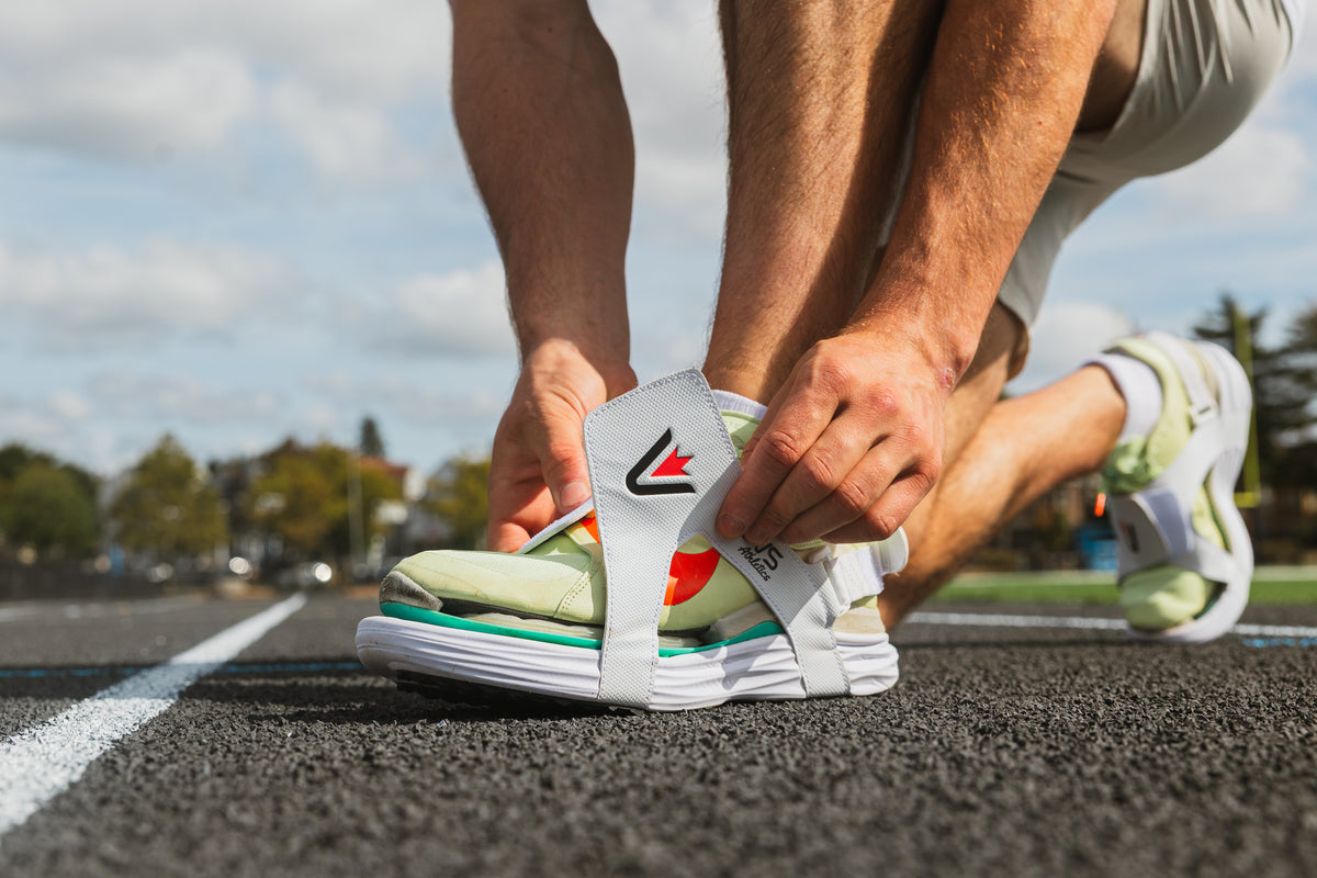 Close-up of an athlete fastening the white strap of a CUVS CV1 Whiteout spike cover over a light green track spike.