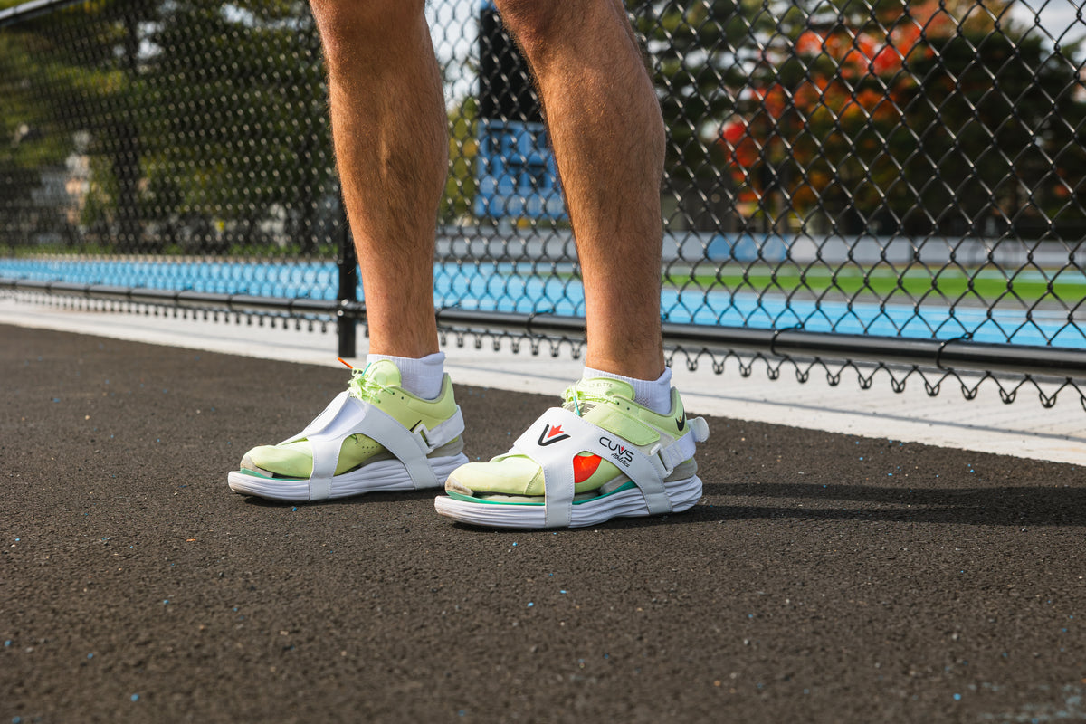 CUVS CV1 Whiteout spike covers worn over light green track spikes on pavement beside a track fence.