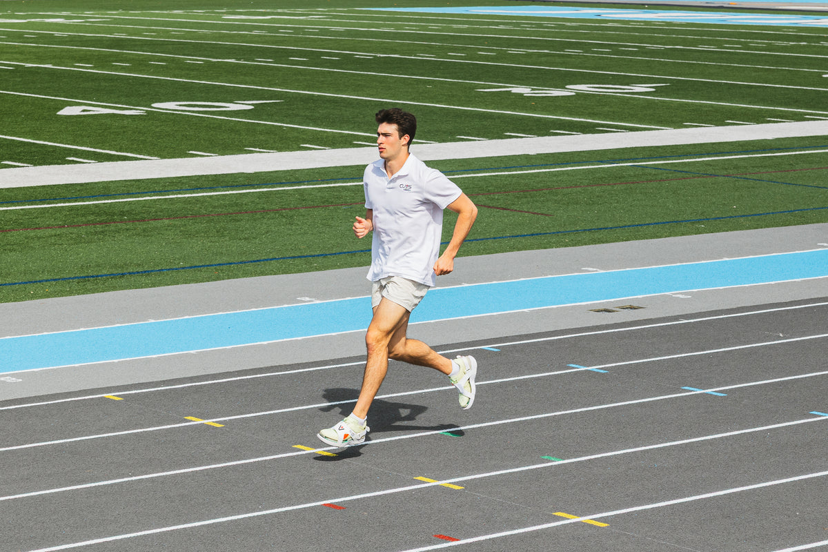 Athlete running in CUVS Whiteout track spike covers during a warmup on an outdoor track.