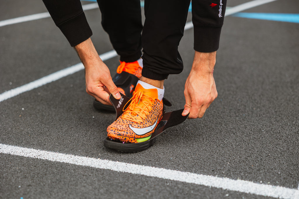 Athlete securing CUVS track spike covers over sprint spikes on an outdoor track.