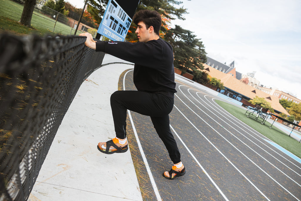 Athlete warming up in CUVS track spike covers beside an outdoor running track.