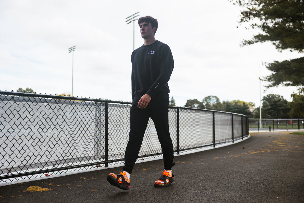 Athlete walking on pavement beside a track in CUVS CV1 Blackout spike covers over orange track spikes