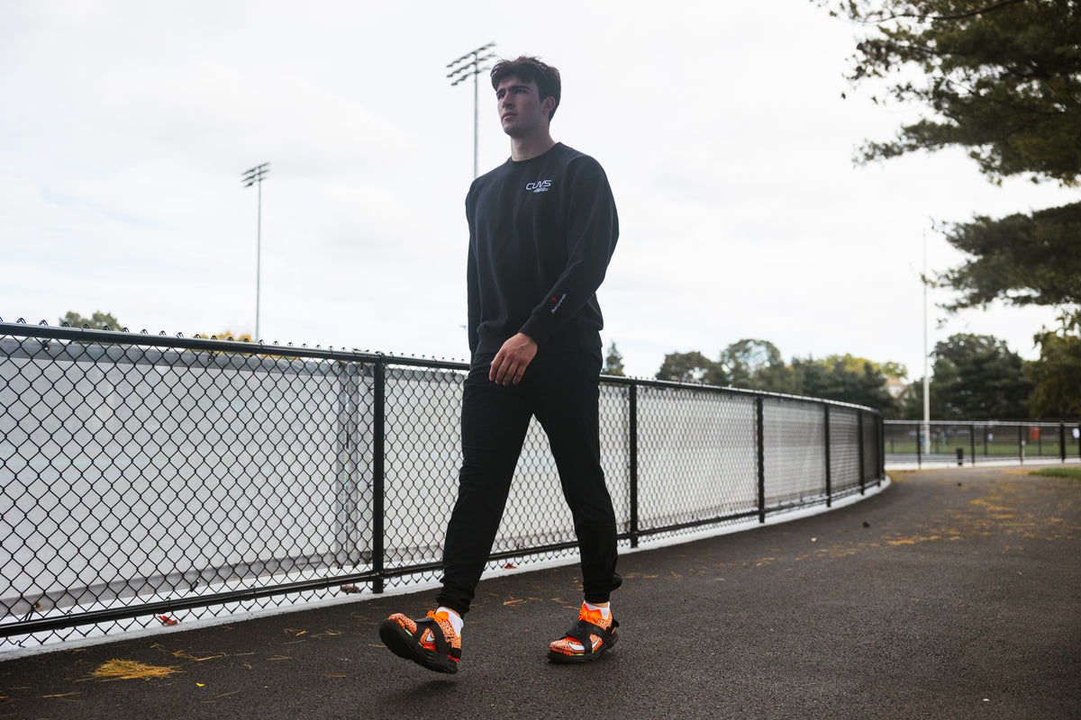 Athlete walking on pavement beside a track in CUVS CV1 Blackout spike covers over orange track spikes